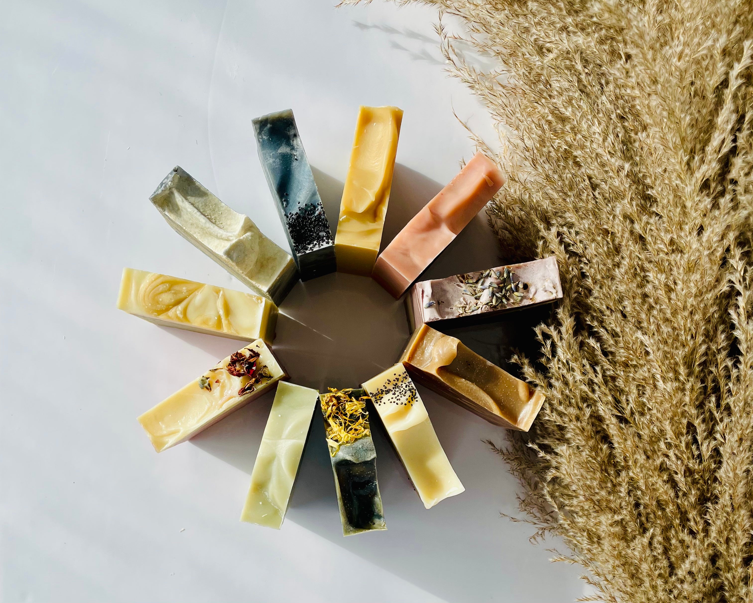 The image shows a bird's eye view of over 10 different soaps arranged in a circular pattern. The soaps are placed in a visually appealing manner, with their different colors and textures visible. The soaps vary in color that is creating an aesthetically pleasing display. The image is linked to an article that showcases the journey of the creator into the world of soap making.